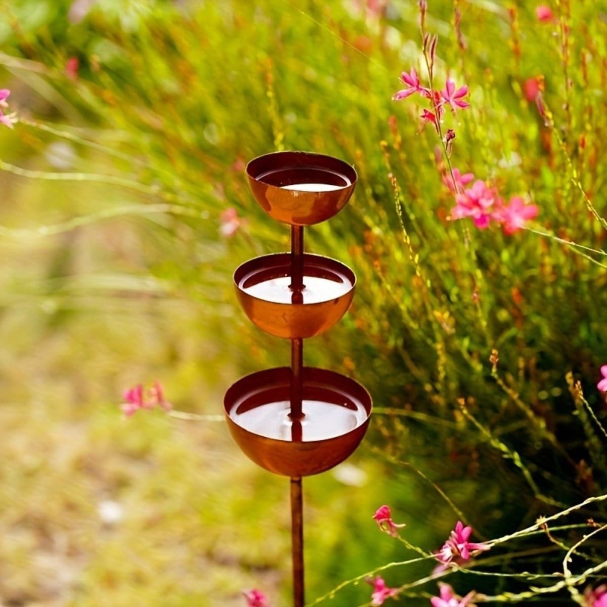 Colonne métallique à trois coupelles d'eau étagées installée dans un massif fleuri